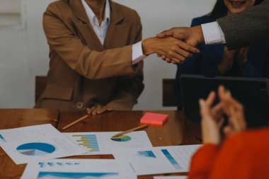 Bir grup iş adamı mutlu ve kendinden emin gülümsüyor. Birlikte çalışırken gülümseyerek ofiste el sıkışırken.