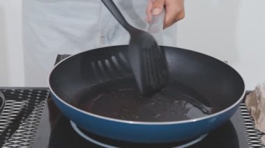 Kadın mutfakta yemek pişiriyor, tavayı hazırlıyor ve karıştırıyor.