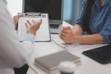 Doktor ve hasta klinikteki ahşap masada yan yana oturuyorlar. Kadın doktor bir kayıt formunu işaret ediyor. Tıp konsepti