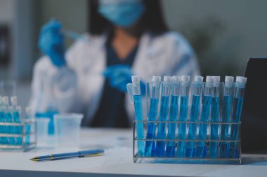 Kendini adamış bir grup bilim adamı tıbbi laboratuvarda kimyasal deney yapıyor. Aşı ilacı veya antibiyotik geliştirmek için pipetten deney tüpüne kesin miktarda sıvı döküyorlar. Neoterik