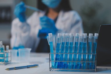 Kendini adamış bir grup bilim adamı tıbbi laboratuvarda kimyasal deney yapıyor. Aşı ilacı veya antibiyotik geliştirmek için pipetten deney tüpüne kesin miktarda sıvı döküyorlar. Neoterik