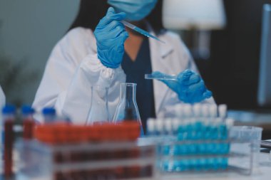 Kendini adamış bir grup bilim adamı tıbbi laboratuvarda kimyasal deney yapıyor. Aşı ilacı veya antibiyotik geliştirmek için pipetten deney tüpüne kesin miktarda sıvı döküyorlar. Neoterik