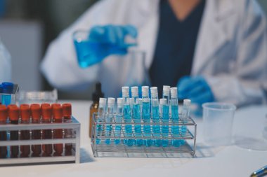 Kendini adamış bir grup bilim adamı tıbbi laboratuvarda kimyasal deney yapıyor. Aşı ilacı veya antibiyotik geliştirmek için pipetten deney tüpüne kesin miktarda sıvı döküyorlar. Neoterik