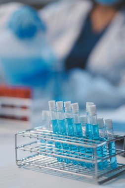 Kendini adamış bir grup bilim adamı tıbbi laboratuvarda kimyasal deney yapıyor. Aşı ilacı veya antibiyotik geliştirmek için pipetten deney tüpüne kesin miktarda sıvı döküyorlar. Neoterik