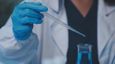 Koruyucu eldivenli bilim adamı laboratuarda sıvı tüp tutuyor.