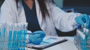Laboratuvarda tüplere bakan koruyucu eldivenli kadın bilim adamının yakın görüntüsü..