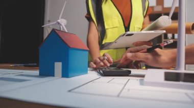 Emlak projesinin planı ve inşaat ofisinin planı üzerinde ev modeliyle çalışan mühendis veya mimar.