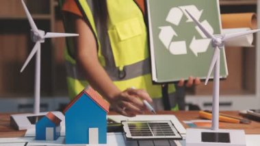 Kadın mühendis elinde yeşil güneş panelleri ve rüzgar türbinleri tutuyor.