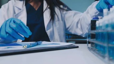 Kadın bilim adamının yakın plan görüntüsü modern laboratuardaki test tüplerini inceliyor.