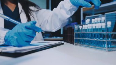 Kadın bilim adamının yakın plan görüntüsü modern laboratuardaki test tüplerini inceliyor.