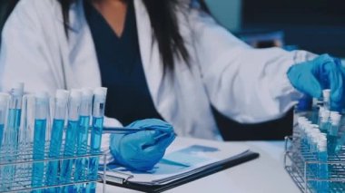 Kadın bilim adamının yakın plan görüntüsü modern laboratuardaki test tüplerini inceliyor.