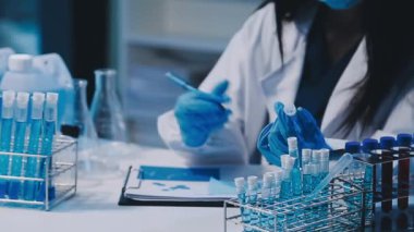 Kadın bilim adamının yakın plan görüntüsü modern laboratuardaki test tüplerini inceliyor.