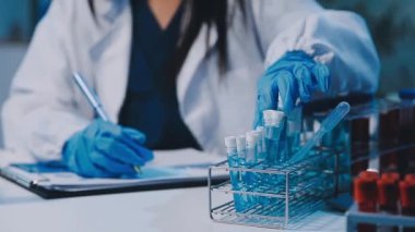 Kadın bilim adamının yakın plan görüntüsü modern laboratuardaki test tüplerini inceliyor.
