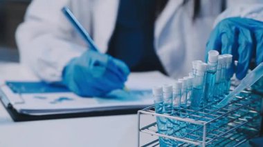 Kadın bilim adamının yakın plan görüntüsü modern laboratuardaki test tüplerini inceliyor.