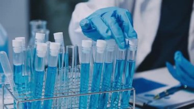 Kadın bilim adamının yakın plan görüntüsü modern laboratuardaki test tüplerini inceliyor.
