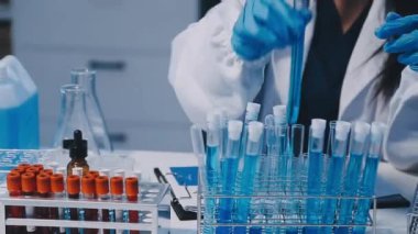 Kadın bilim adamının yakın plan görüntüsü modern laboratuardaki test tüplerini inceliyor.