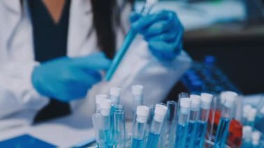 Kadın bilim adamının yakın plan görüntüsü modern laboratuardaki test tüplerini inceliyor.