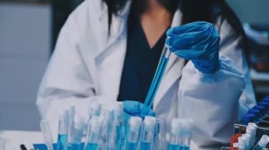 Kadın bilim adamının yakın plan görüntüsü modern laboratuardaki test tüplerini inceliyor.