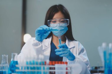 Kendini adamış bir grup bilim adamı tıbbi laboratuvarda kimyasal deney yapıyor. Aşı ilacı veya antibiyotik geliştirmek için pipetten deney tüpüne kesin miktarda sıvı döküyorlar. Neoterik