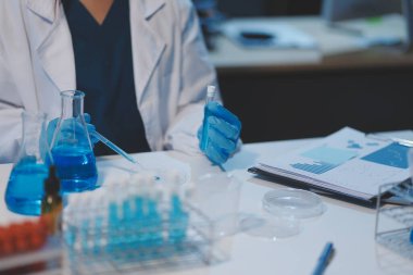 Kendini adamış bir grup bilim adamı tıbbi laboratuvarda kimyasal deney yapıyor. Aşı ilacı veya antibiyotik geliştirmek için pipetten deney tüpüne kesin miktarda sıvı döküyorlar. Neoterik