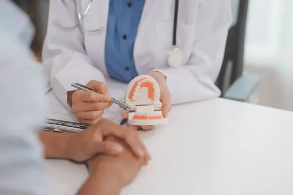 Diş hekimi muayenesi. Diş hekimliği muayenehanesine hasta ziyareti. Diş tellerini açıklamak için takma diş takan kadın diş hekimi hastanın durumu hakkında tavsiye veren ortodonti diş hekimi için kılavuz öneriyor.