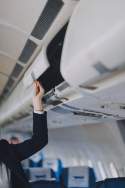 Asyalı kadın turist bavulunu uçağın içindeki bir rafa koyar..