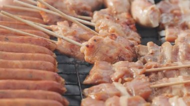 Şişler üzerinde ızgara yapılan ve yanında sosis kızaran tavuk satayının detaylı görüntüsü..