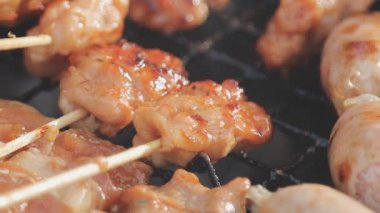 Şişler üzerinde ızgara yapılan ve yanında sosis kızaran tavuk satayının detaylı görüntüsü..