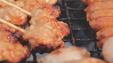 Şişler üzerinde ızgara yapılan ve yanında sosis kızaran tavuk satayının detaylı görüntüsü..