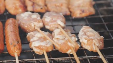 Şişler üzerinde ızgara yapılan ve yanında sosis kızaran tavuk satayının detaylı görüntüsü..