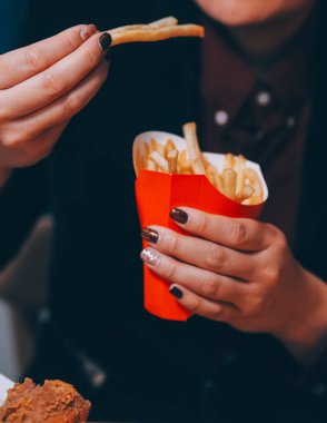Asyalı kadın elinde patates kızartması ve restoranda mutlu bir şekilde yemek yiyor.