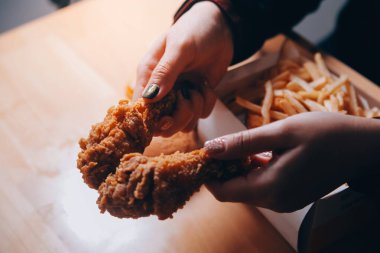 Odaklan kadın. Elin kızarmış tavuğu yemek için tutuyor. Fast food konsepti olan bir kız.