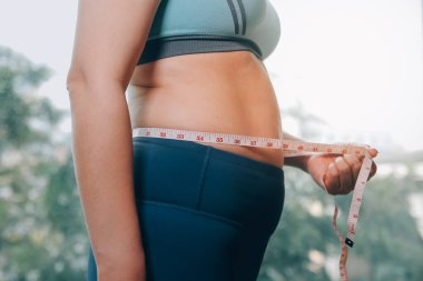 Şişman kadın, şişko, obez kadın el ele tutuşan ölçü bandıyla göbek yağı, kadın diyeti yaşam tarzı konsepti