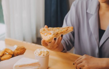 Restoranda pizza dilimi tutan bir kadın resmi.