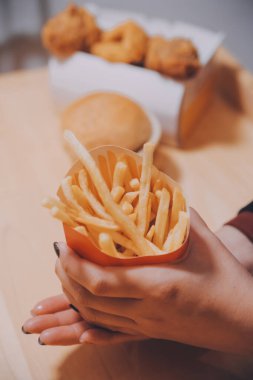 Asyalı kadın elinde patates kızartması ve restoranda mutlu bir şekilde yemek yiyor.