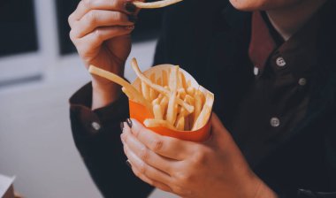 Asyalı kadın elinde patates kızartması ve restoranda mutlu bir şekilde yemek yiyor.