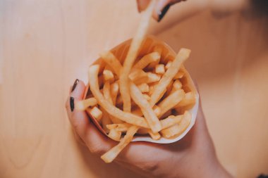 Asyalı kadın elinde patates kızartması ve restoranda mutlu bir şekilde yemek yiyor.