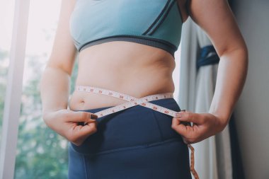 Şişman kadın, şişko, obez kadın el ele tutuşan ölçü bandıyla göbek yağı, kadın diyeti yaşam tarzı konsepti