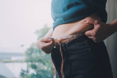 Şişman kadın, şişko, obez kadın el ele tutuşan ölçü bandıyla göbek yağı, kadın diyeti yaşam tarzı konsepti