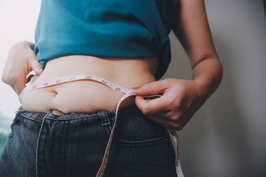 Şişman kadın, şişko, obez kadın el ele tutuşan ölçü bandıyla göbek yağı, kadın diyeti yaşam tarzı konsepti