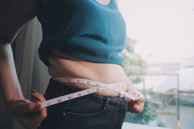 Şişman kadın, şişko, obez kadın el ele tutuşan ölçü bandıyla göbek yağı, kadın diyeti yaşam tarzı konsepti