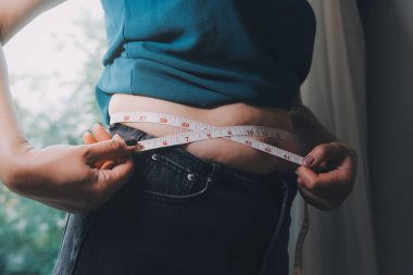 Şişman kadın, şişko, obez kadın el ele tutuşan ölçü bandıyla göbek yağı, kadın diyeti yaşam tarzı konsepti