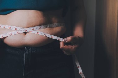 Şişman kadın, şişko, obez kadın el ele tutuşan ölçü bandıyla göbek yağı, kadın diyeti yaşam tarzı konsepti