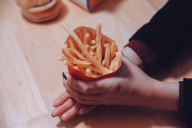 Asyalı kadın elinde patates kızartması ve restoranda mutlu bir şekilde yemek yiyor.