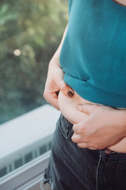 Şişman kadın, şişko, obez kadın el ele tutuşan ölçü bandıyla göbek yağı, kadın diyeti yaşam tarzı konsepti