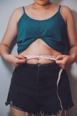 Şişman kadın, şişko, obez kadın el ele tutuşan ölçü bandıyla göbek yağı, kadın diyeti yaşam tarzı konsepti