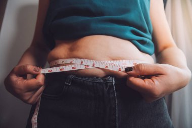 Şişman kadın, şişko, obez kadın el ele tutuşan ölçü bandıyla göbek yağı, kadın diyeti yaşam tarzı konsepti