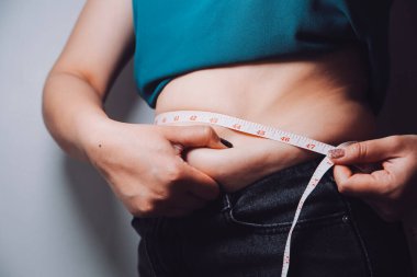 Şişman kadın, şişko, obez kadın el ele tutuşan ölçü bandıyla göbek yağı, kadın diyeti yaşam tarzı konsepti