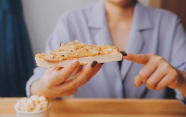 Restoranda pizza dilimi tutan bir kadın resmi.