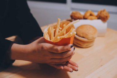 Asyalı kadın elinde patates kızartması ve restoranda mutlu bir şekilde yemek yiyor.